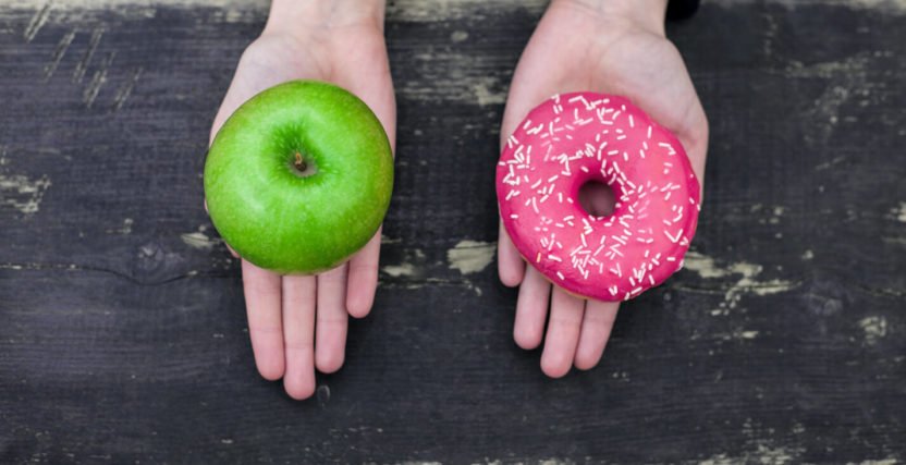 One hand holding a donut and one hand holding an apple