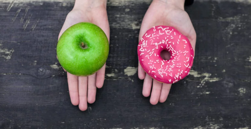 One hand holding a donut and one hand holding an apple